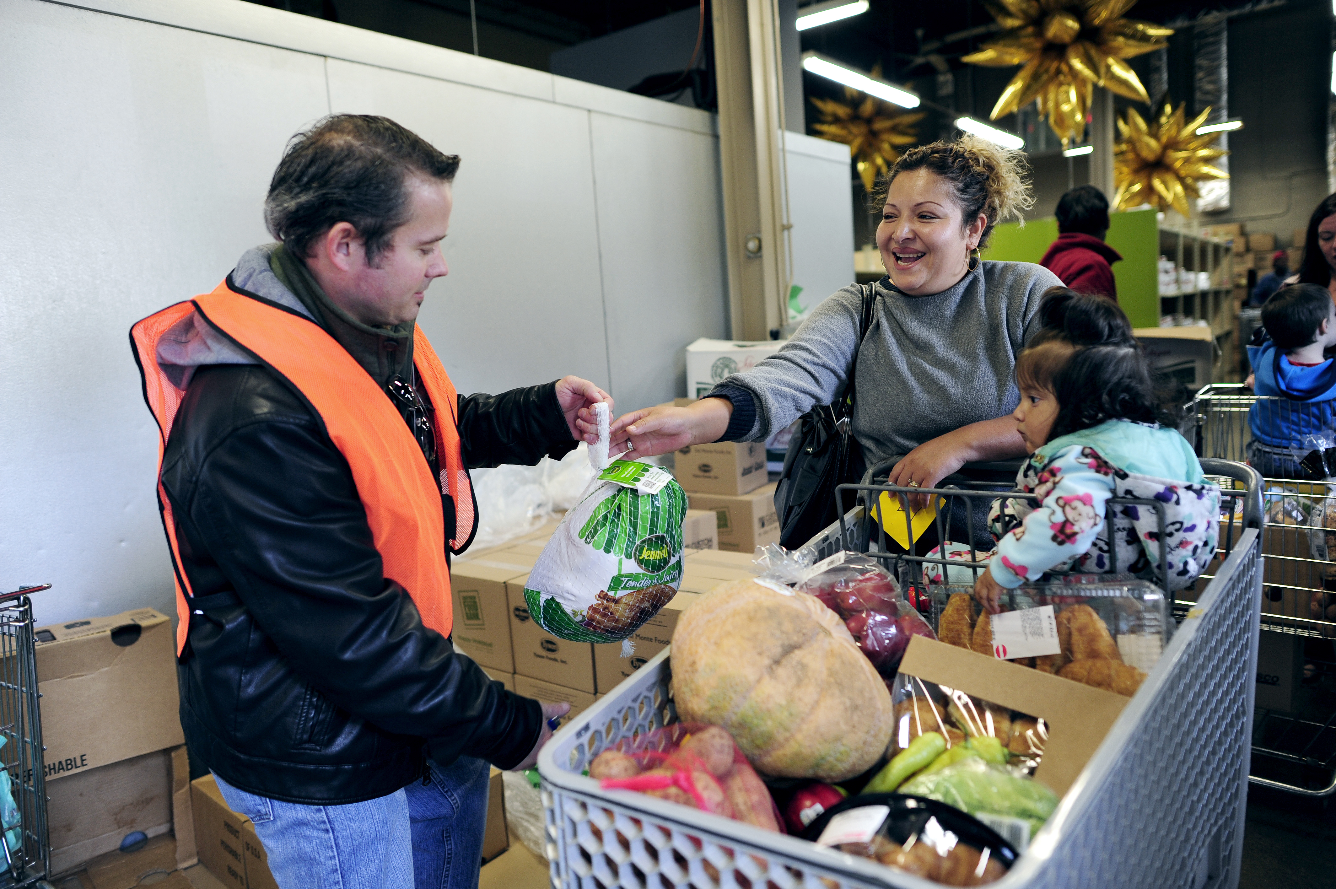 Image of a woman pushing a shopping cart and a man handing her groceries.