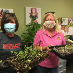 image of two people inside holding pots and small plants.