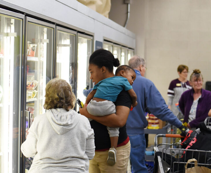 Image of a woman and child being helped by a volunteer at the freezer section inside the Aurora Food Pantry.