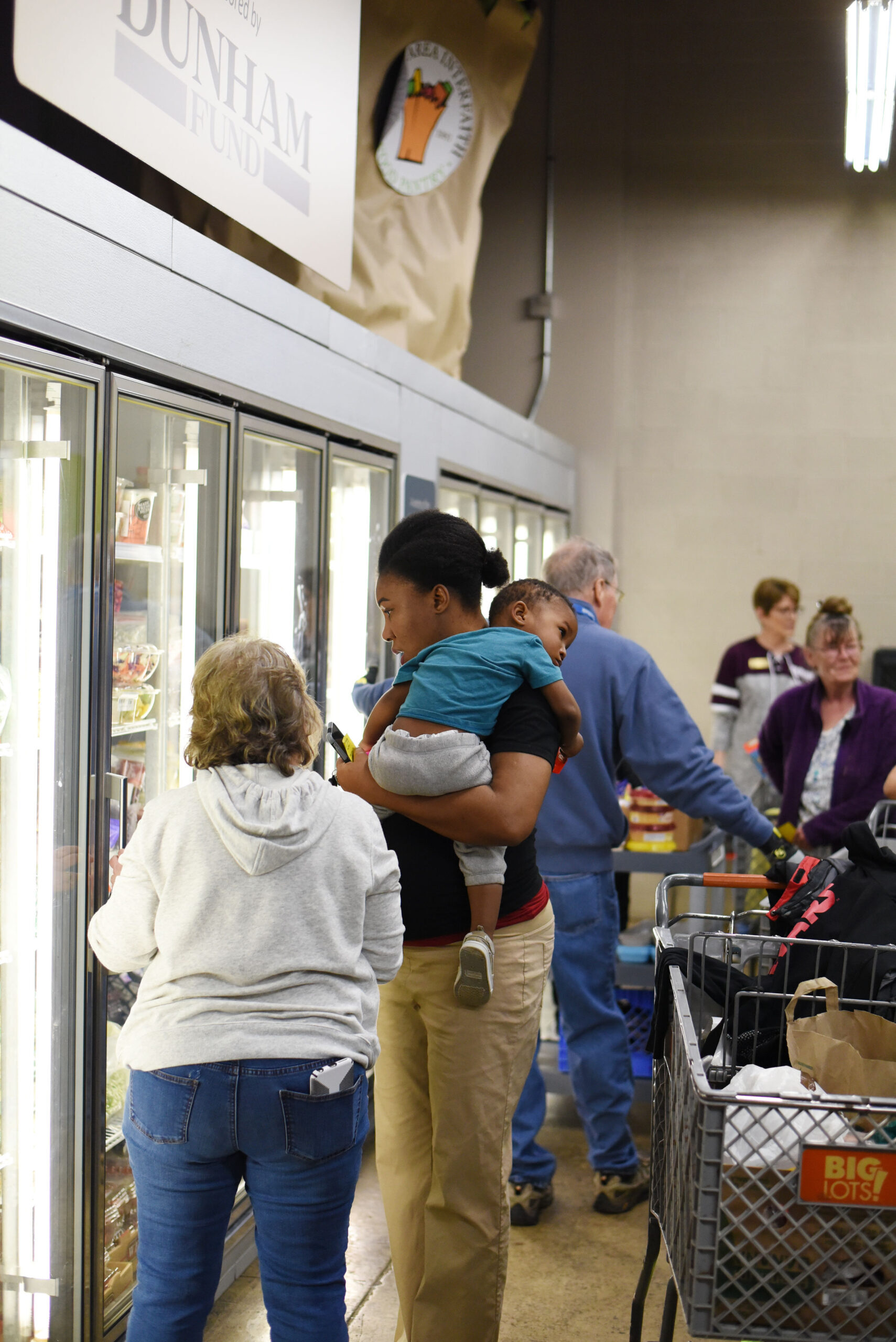 Image of a woman and child being helped by a volunteer at the freezer section inside the Aurora Food Pantry.