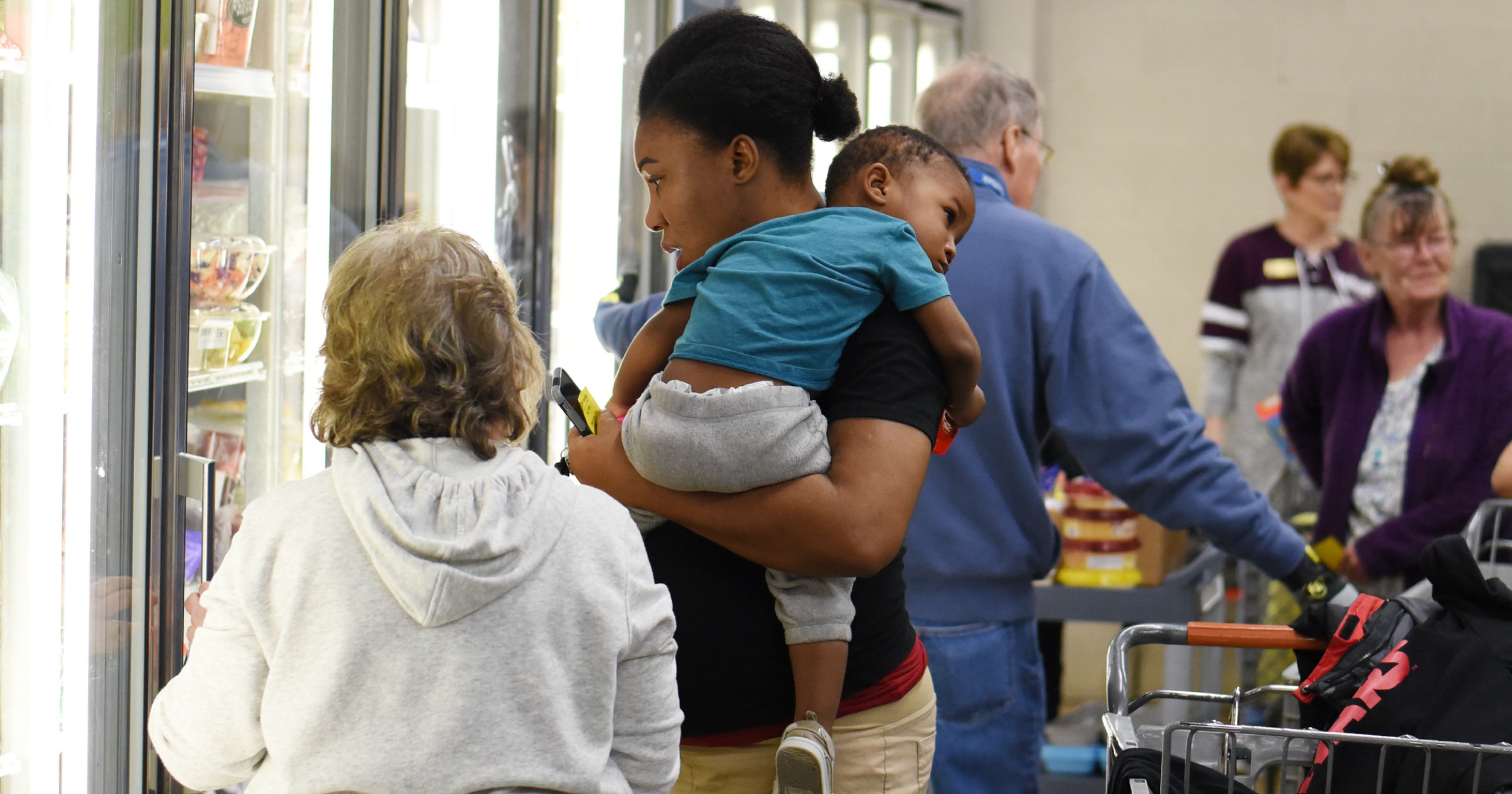 Image of woman holding a child and looking into fridge.