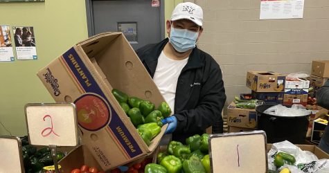 Image of man in a mask holding a box of veggies near produce section at the Aurora Area Interfaith Food Pantry
